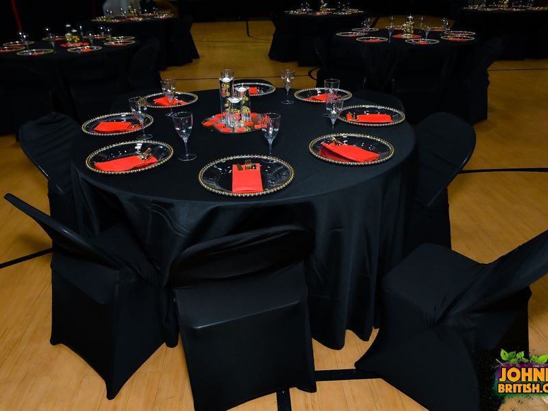 Round guest table rental with floor-length black linens, black spandex chair covers, gold-beaded charger plates, red napkins, and a mirrored floating candle centerpiece at a Long Island birthday party