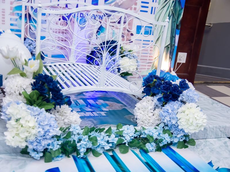 Blue and white floral installation with hydrangea clusters, navy blue roses, white tulips, and trailing greenery framing a white iron bridge at a Long Island themed event