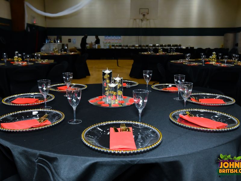 Close-up of a black, red, and gold place setting with a gold-beaded charger plate, folded red napkin, gold flatware, and a mirrored floating candle centerpiece at a Nassau County event